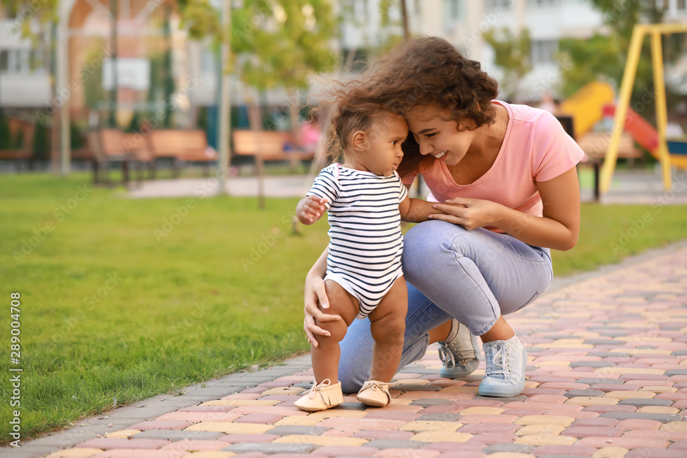 African-American mother teaching her little baby to walk outdoors