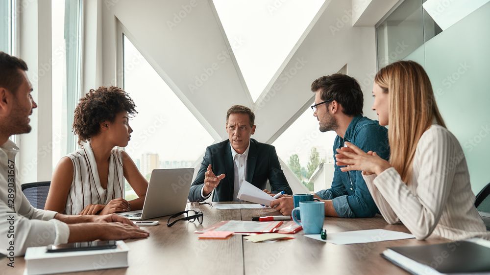 Staff meeting. Serious mature man discussing new project with his multicultural team while sitting a