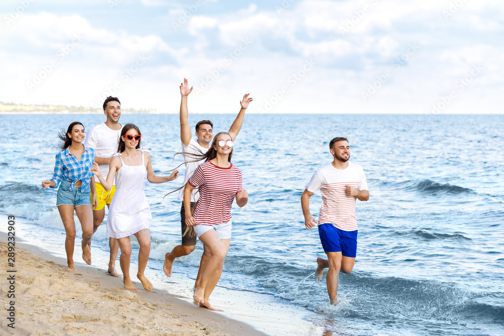 Happy friends running on sea beach at resort