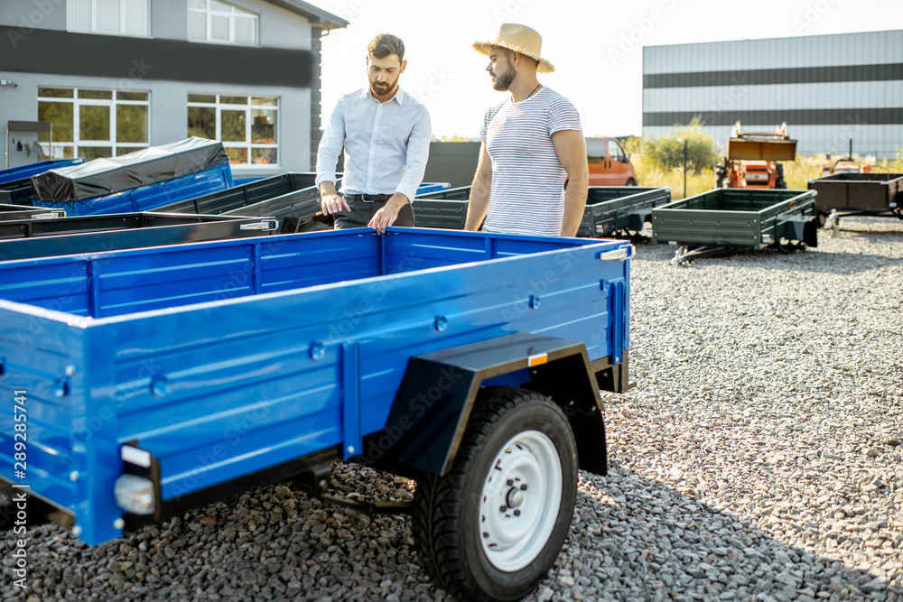 Agronomist with salesman choosing a new farm truck trailer, standing on the open ground of the agric