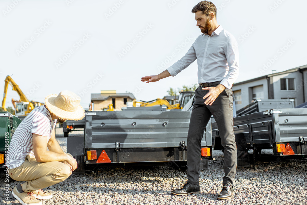 Agronomist with salesman choosing a new farm truck trailer, standing on the open ground of the agric