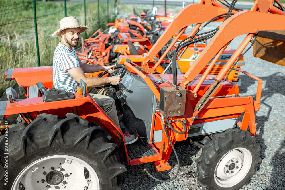 Young agronomist trying tractor for farming, choosing agricultural machinery on the open ground of t