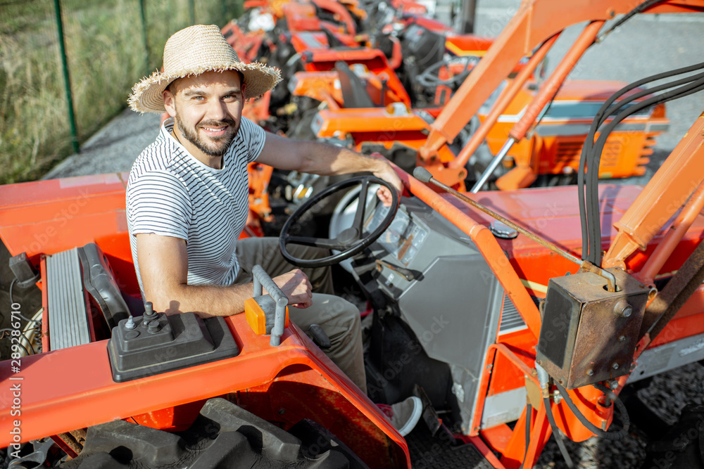 Young agronomist trying tractor for farming, choosing agricultural machinery on the open ground of t