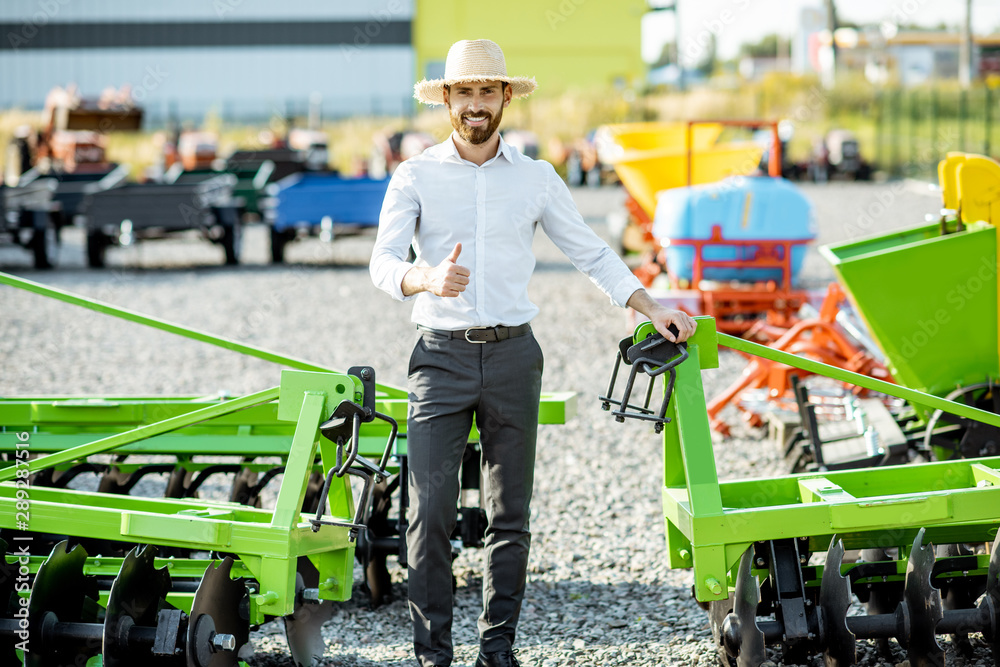 Portrait of a handsome salesman or farmer with straw head standing near the plow at the outdoor grou