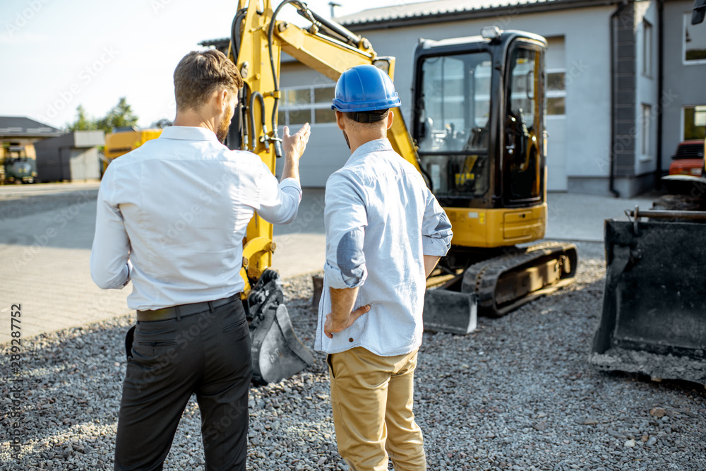 Builder choosing heavy machinery for construction with a sales consultant on the open ground of a sh