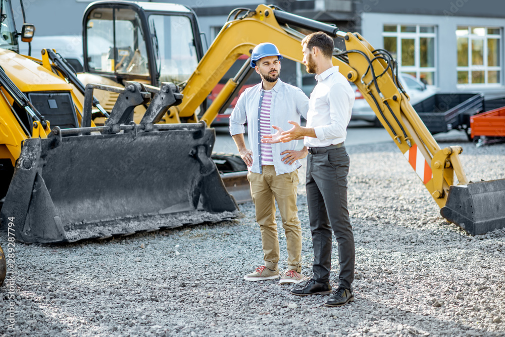 Builder choosing heavy machinery for construction with a sales consultant on the open ground of a sh