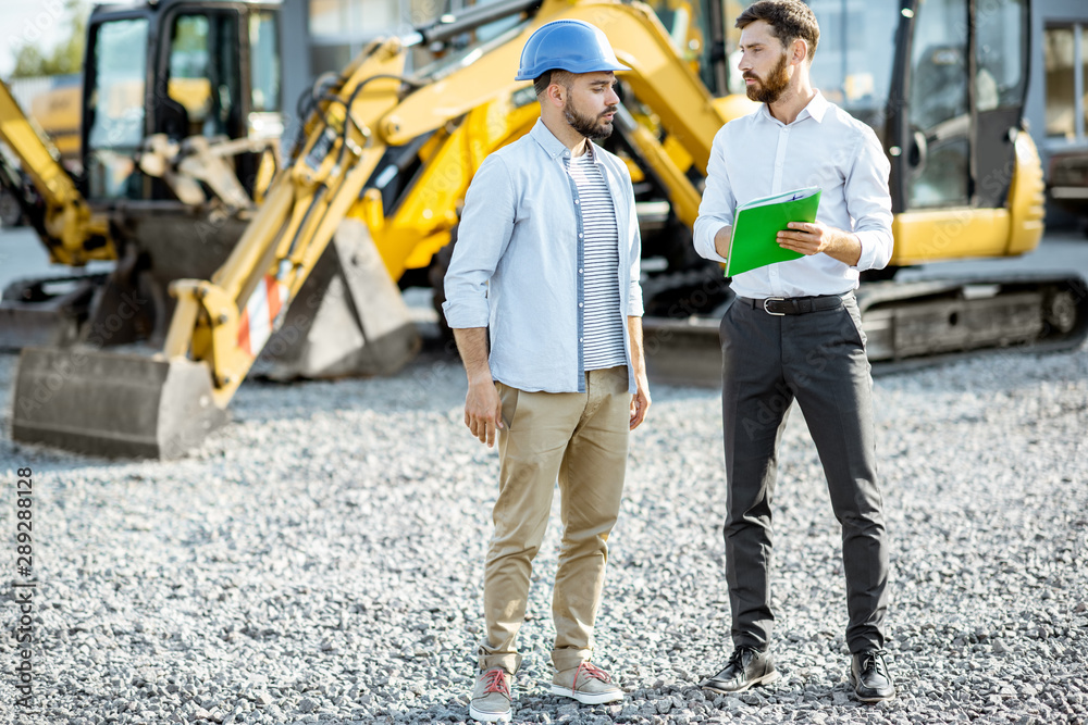 Builder choosing heavy machinery for construction with a sales consultant standing with some documen