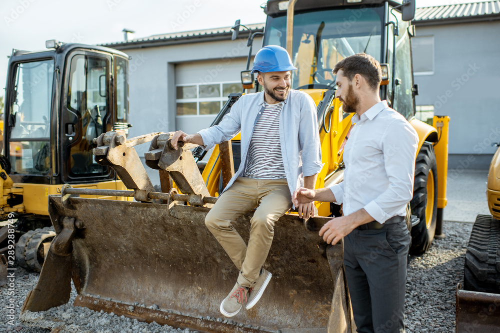 Builder choosing heavy machinery for construction, talking with a sales consultant on the open groun