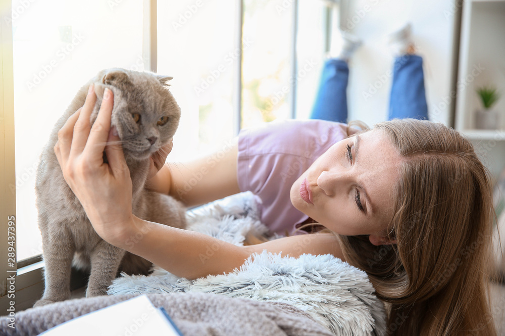 Beautiful woman with cute cat near window at home