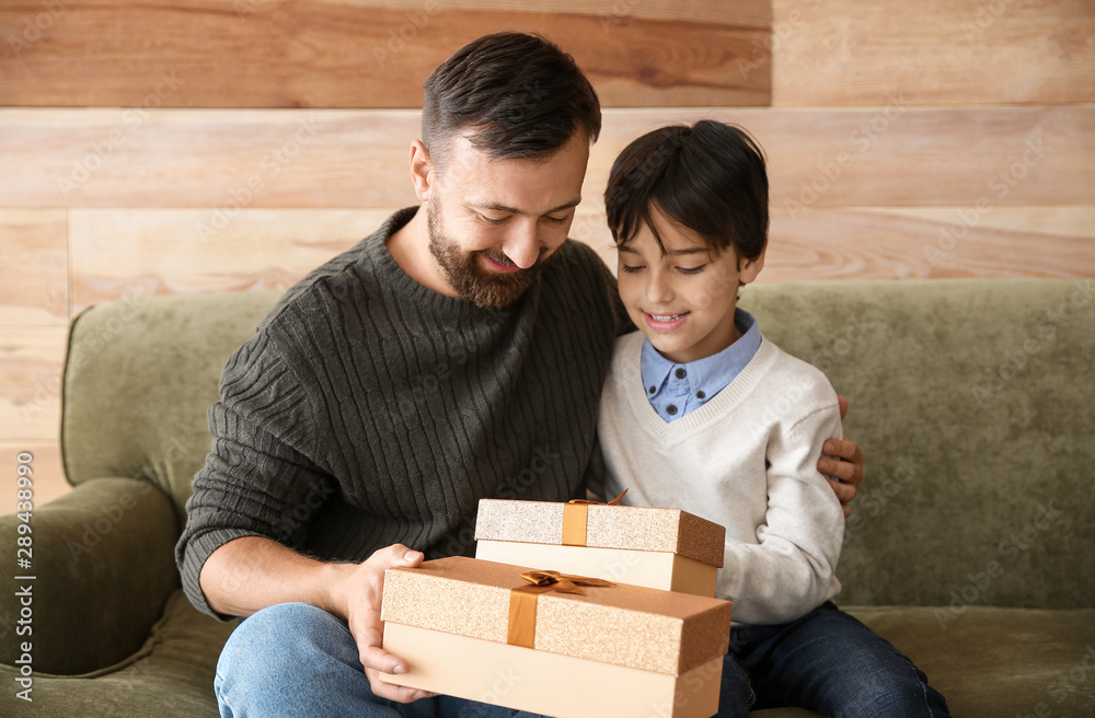 Happy man and his son with Christmas gifts sitting on sofa