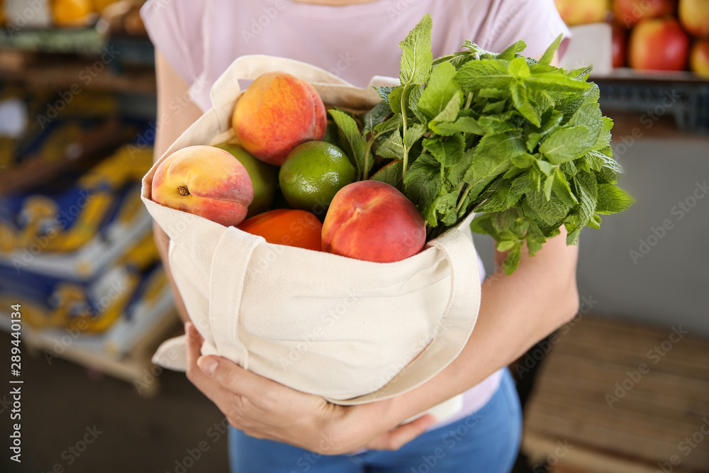 Woman with fresh fruits and herbs in tote bag at market