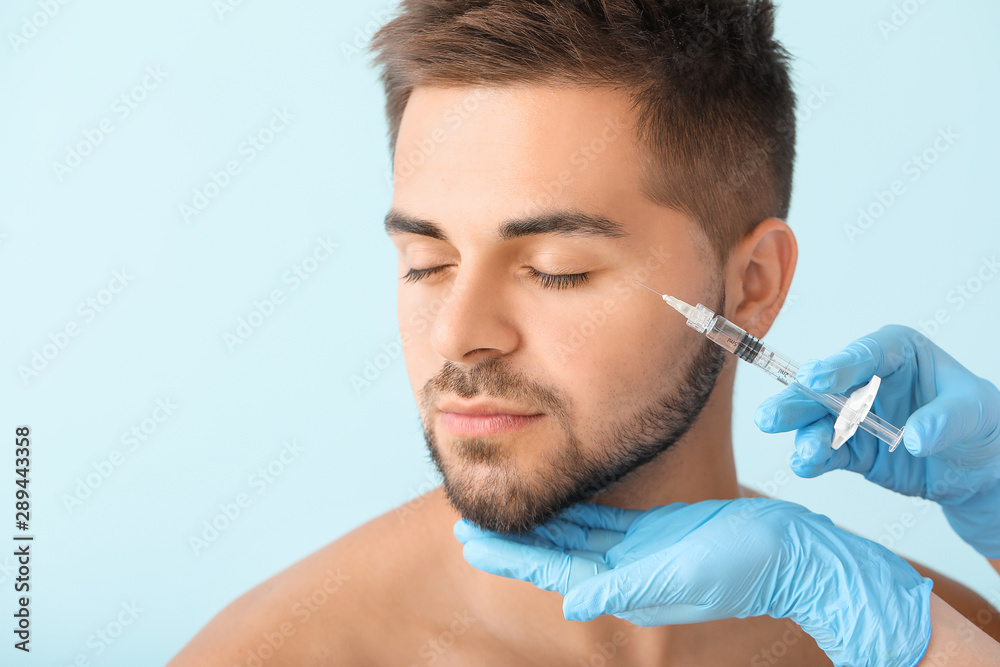 Handsome man receiving filler injection on color background