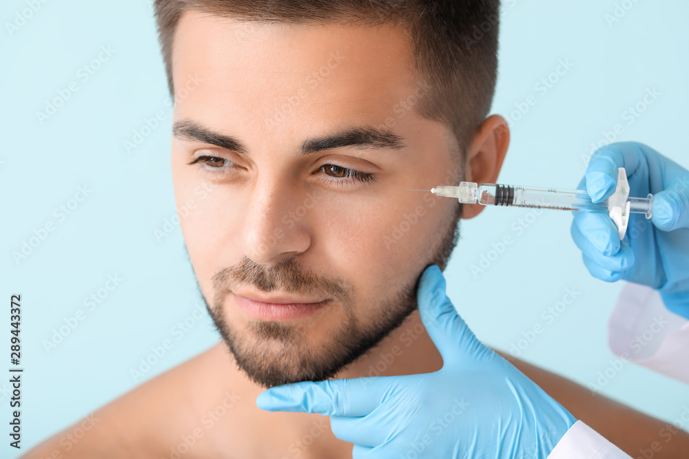 Handsome man receiving filler injection on color background