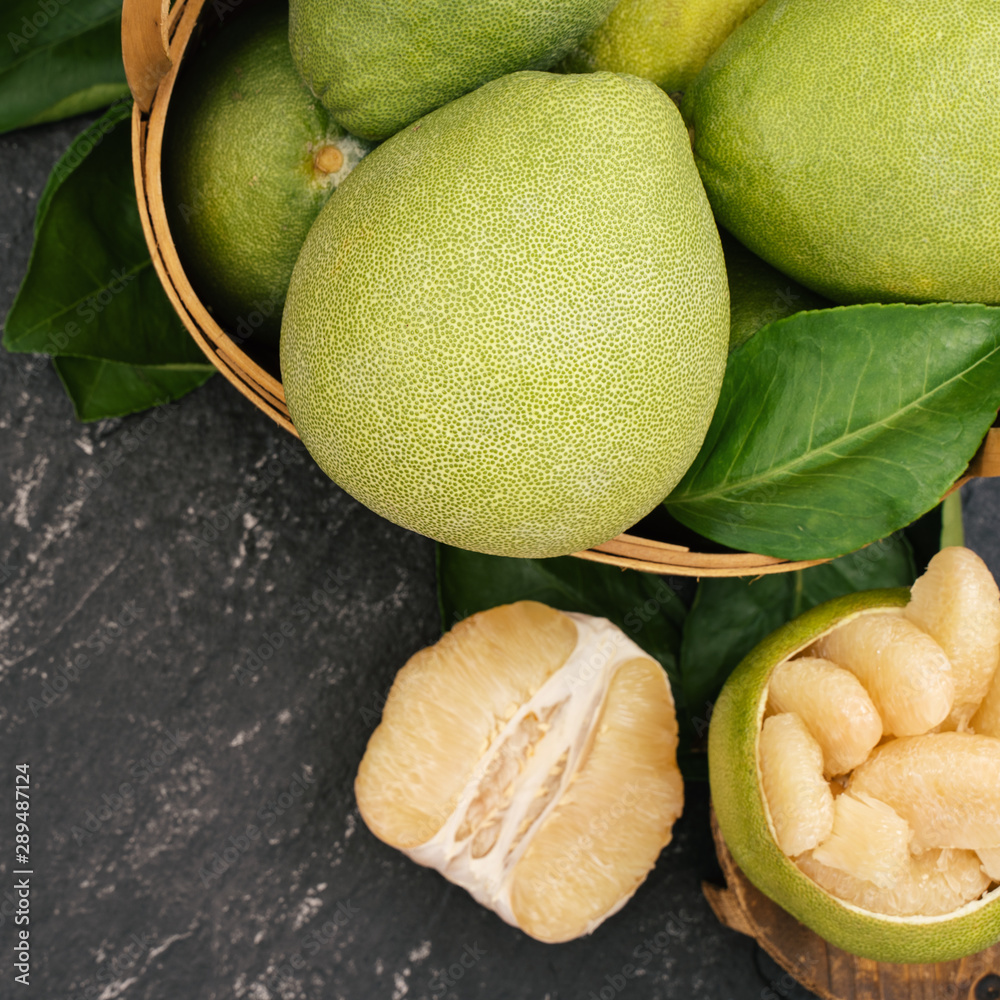 Fresh pomelo, pummelo, grapefruit, shaddock in bamboo basket with leaf on dark black slate backgroun