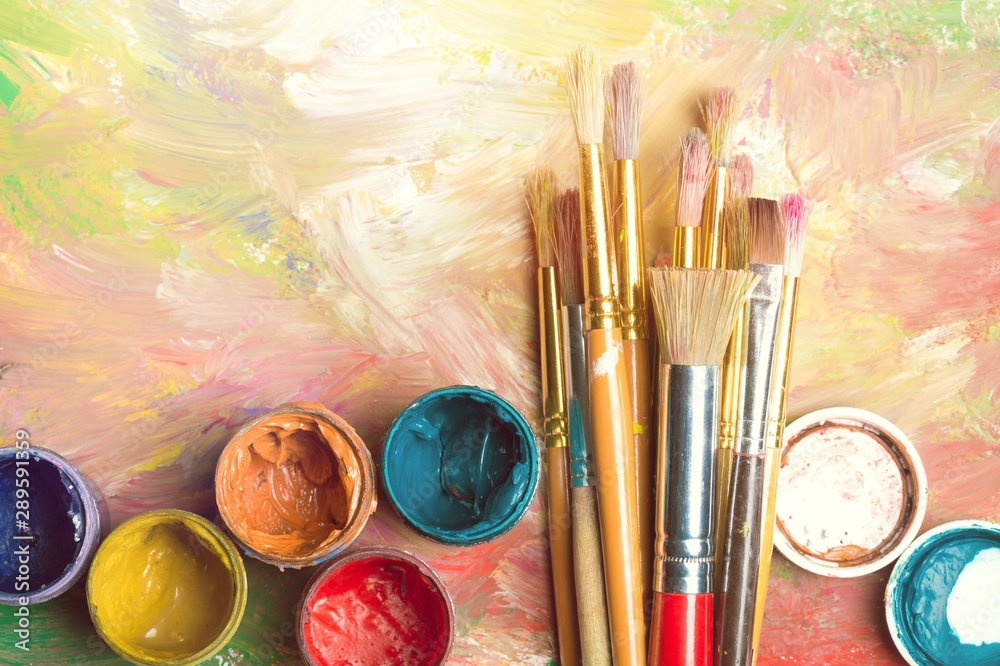 Artist paintbrushes and paint cans of paint over a bright watercolor background