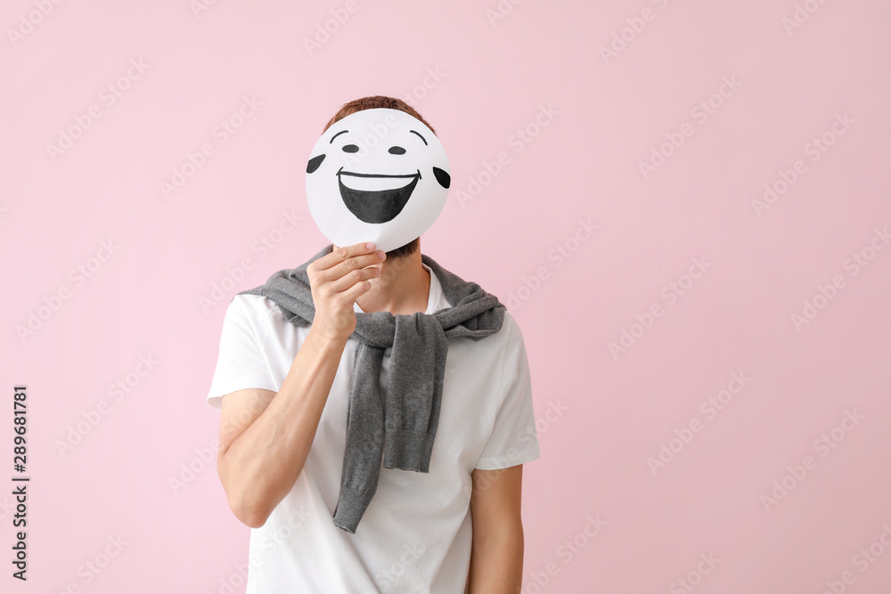 Man hiding face behind sheet of paper with drawn emoticon on color background