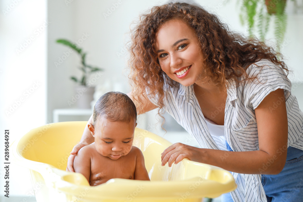 Young African-American mother washing her baby at home