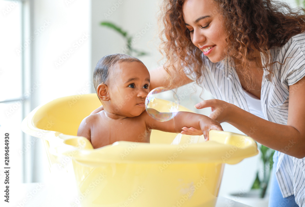 Young African-American mother washing her baby at home