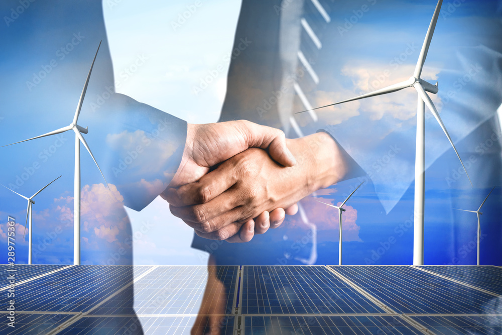 Double exposure graphic of business people handshake over wind turbine farm and green renewable ener