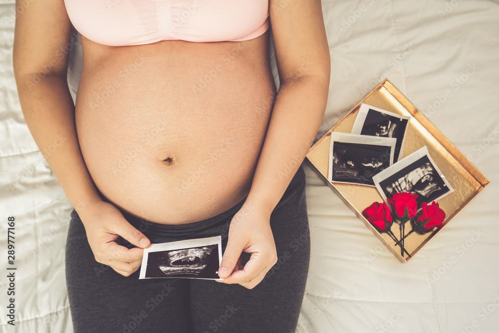 Pregnant woman feeling happy at home while taking care of her child. The young expecting mother hold