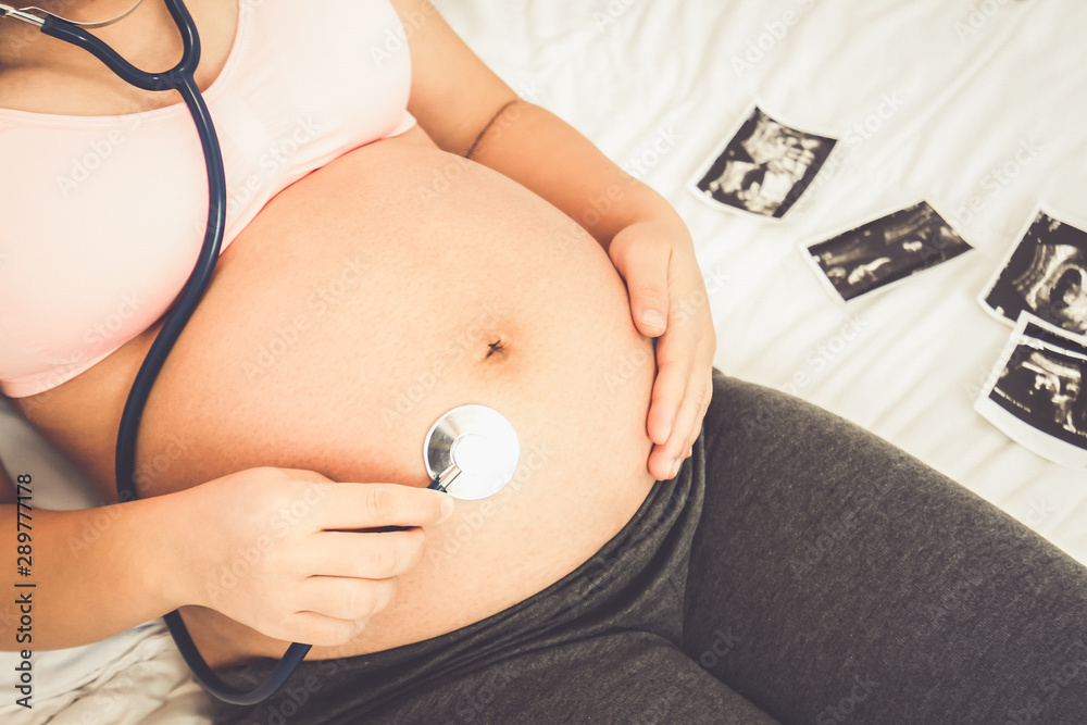 Pregnant woman feeling happy at home while taking care of her child. The young expecting mother hold