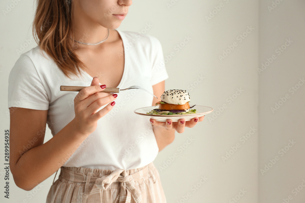 年轻女子在浅色背景下吃美味沙拉