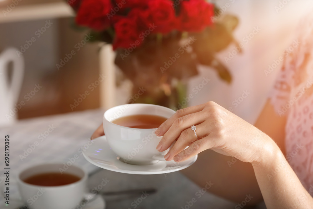 Young woman with engagement ring on her finger drinking tea, closeup