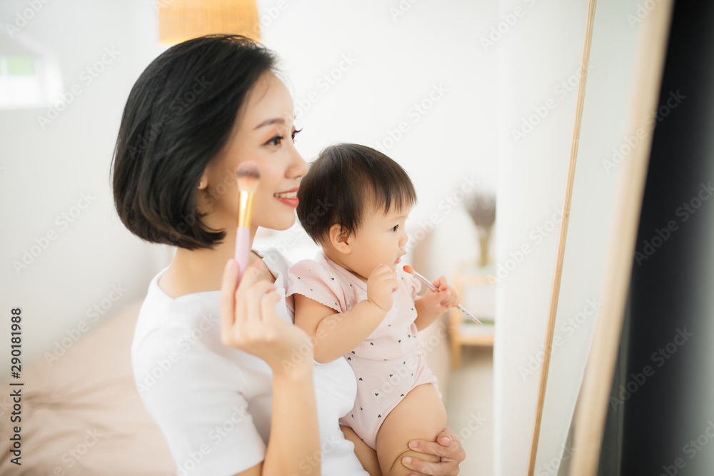 家里有个有趣的家庭。妈妈和她的小女儿正在化妆，在镜子附近玩得很开心。巴