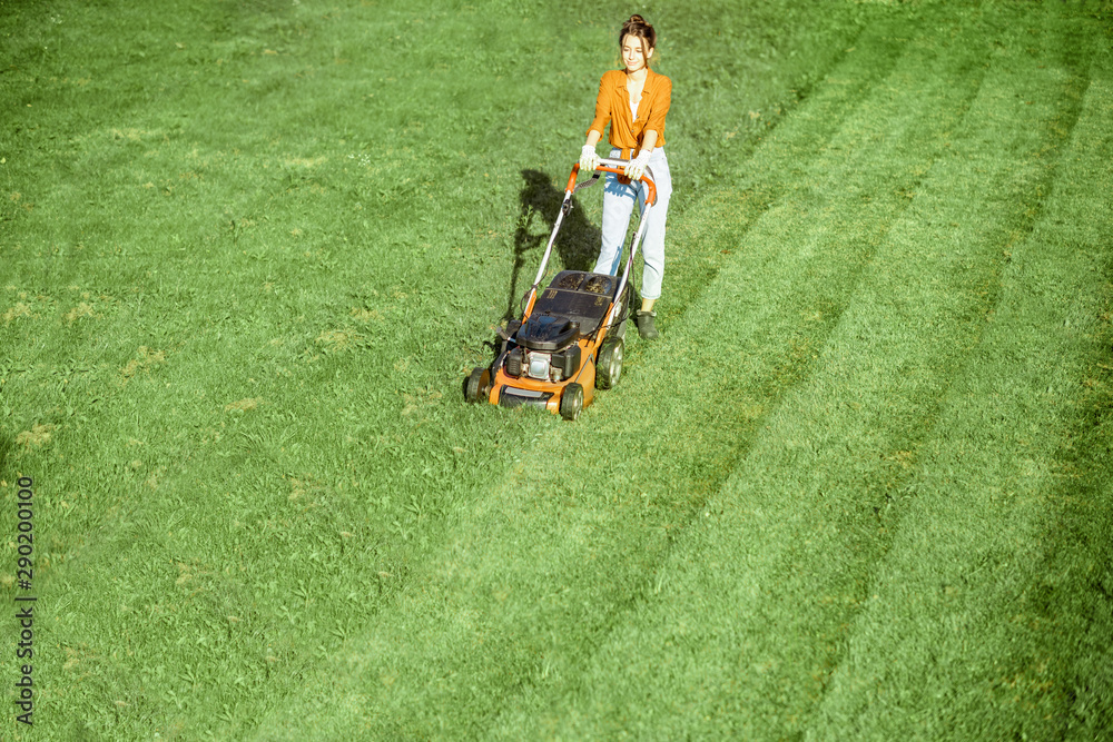 Beautiful young woman cutting grass with gasoline lawn mower, gardening on the backyard in the count