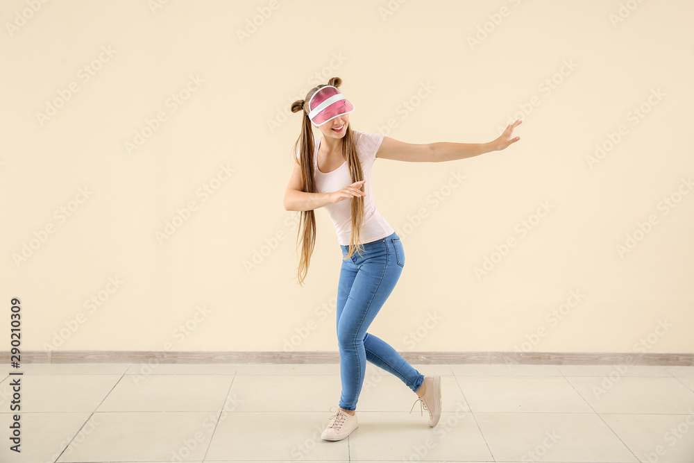 Cool young woman dancing against light wall