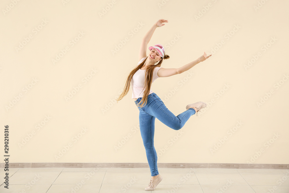 Cool young woman dancing against light wall