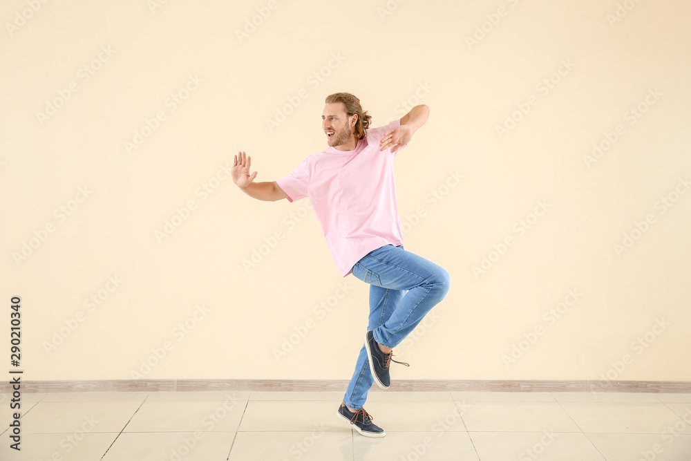 Cool young man dancing against light wall