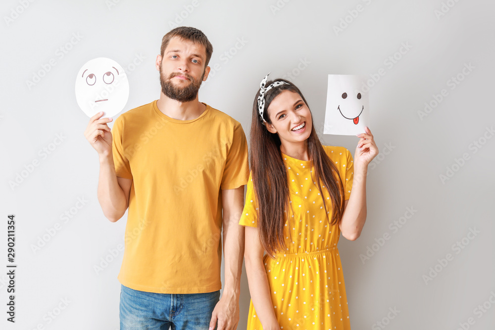 Happy couple holding sheets of paper with drawn emoticons on grey background