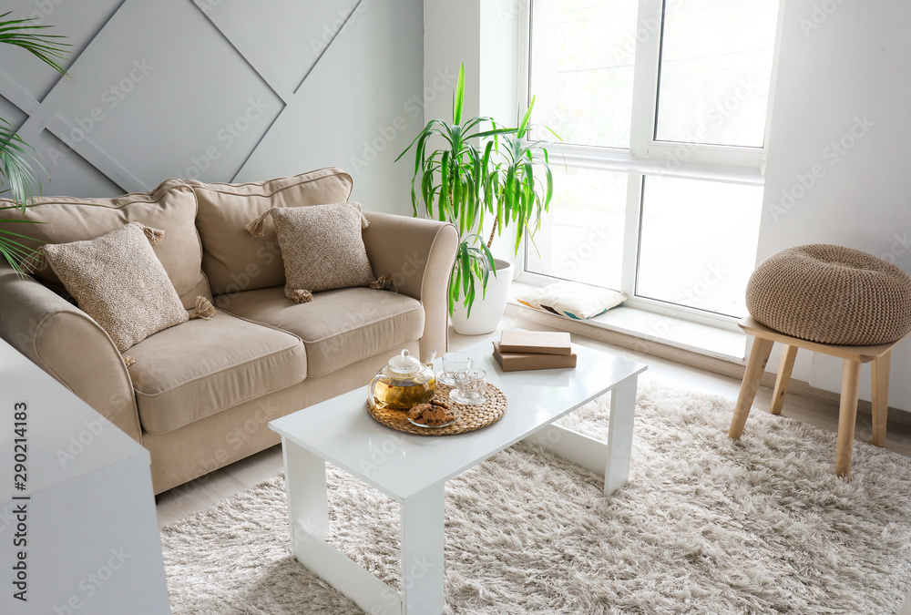 Cozy sofa with table and tropical plant in stylish interior of room