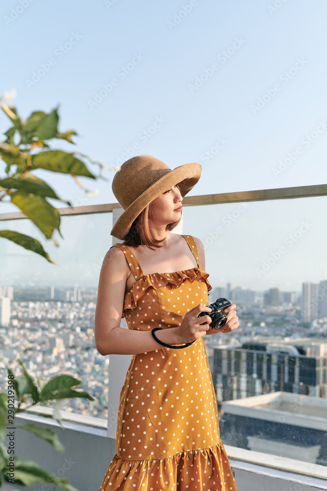 年轻的亚洲女孩站在屋顶上，用相机拍照。夏天的概念。