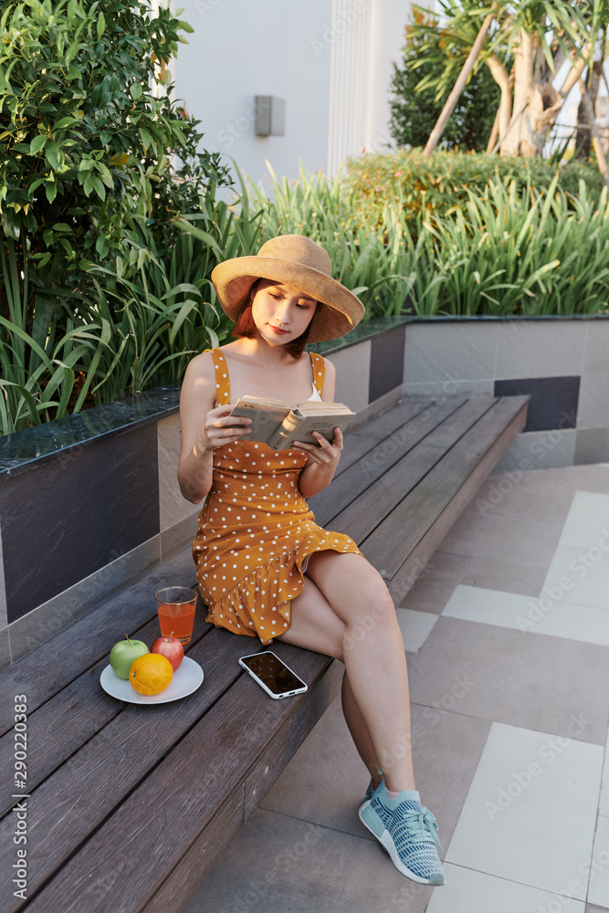 Asian young woman sitting behind a tree reading a book in the park