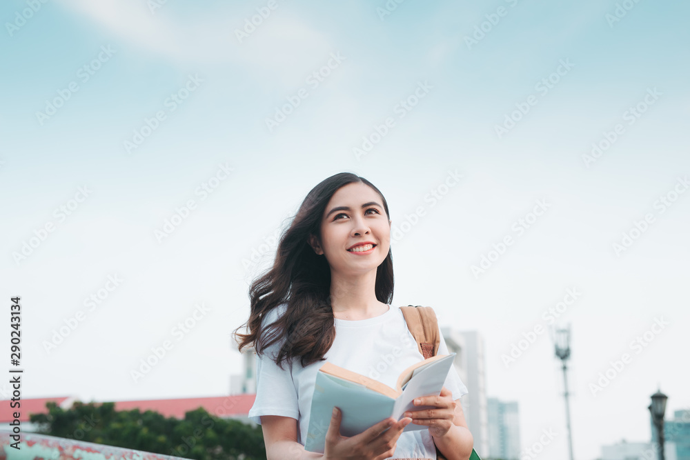 亚洲商务女性旅行，站在栏杆桥旁，阅读城市背景的书籍。