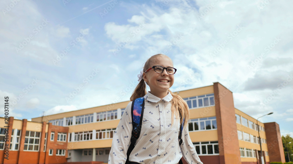 Happy eleven-year schoolgirl runs with a backpack and exercise books after school.