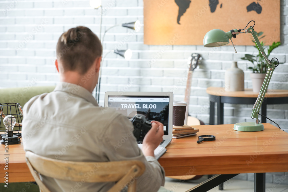 Male travel blogger with laptop at table