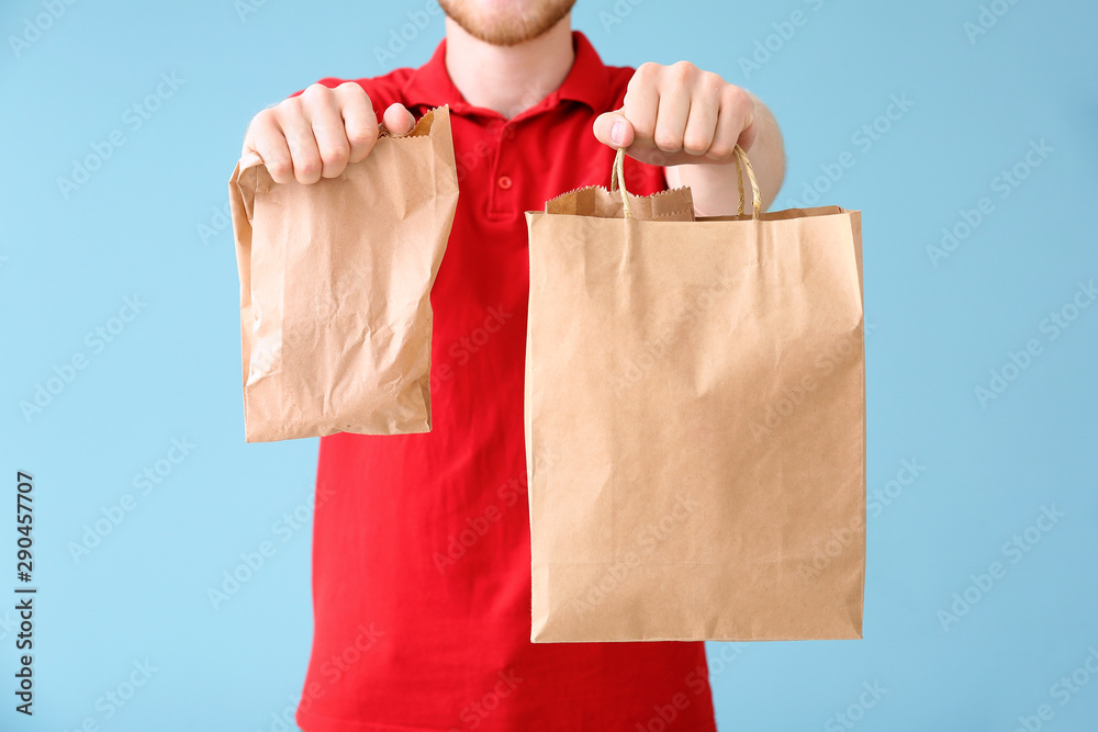 Handsome worker of food delivery service on color background