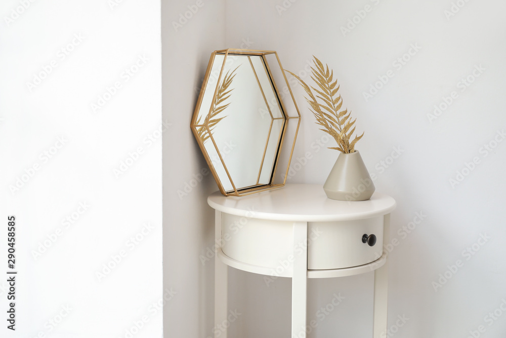 Mirror and vase with golden tropical leaves on table near white wall