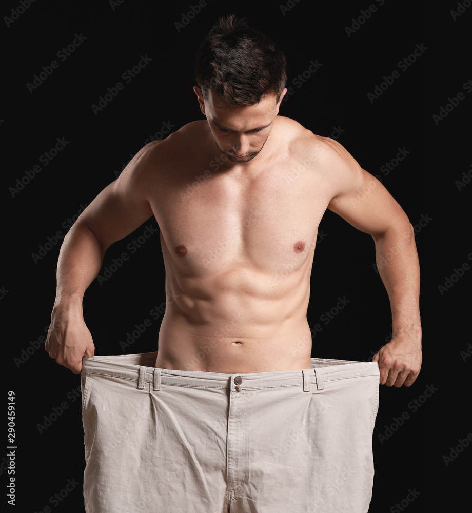 Handsome muscular man in loose pants on dark background. Weight loss concept