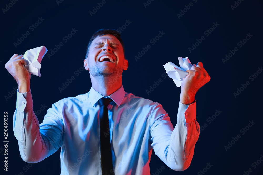 Portrait of angry businessman with crumpled paper on dark background