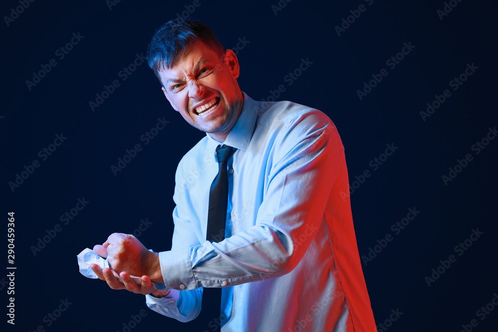 Portrait of angry businessman with crumpled paper on dark background