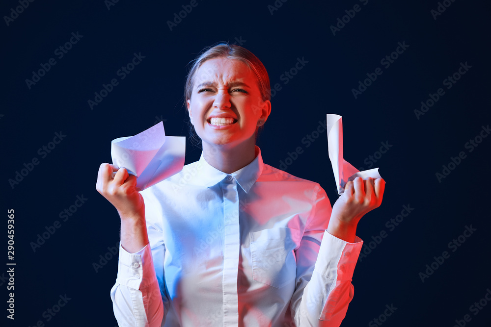 Portrait of angry businesswoman with crumpled paper on dark background