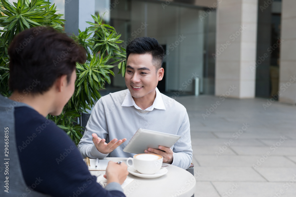 Business people looking at document and discussing while at cafe. Two businessmen working together o