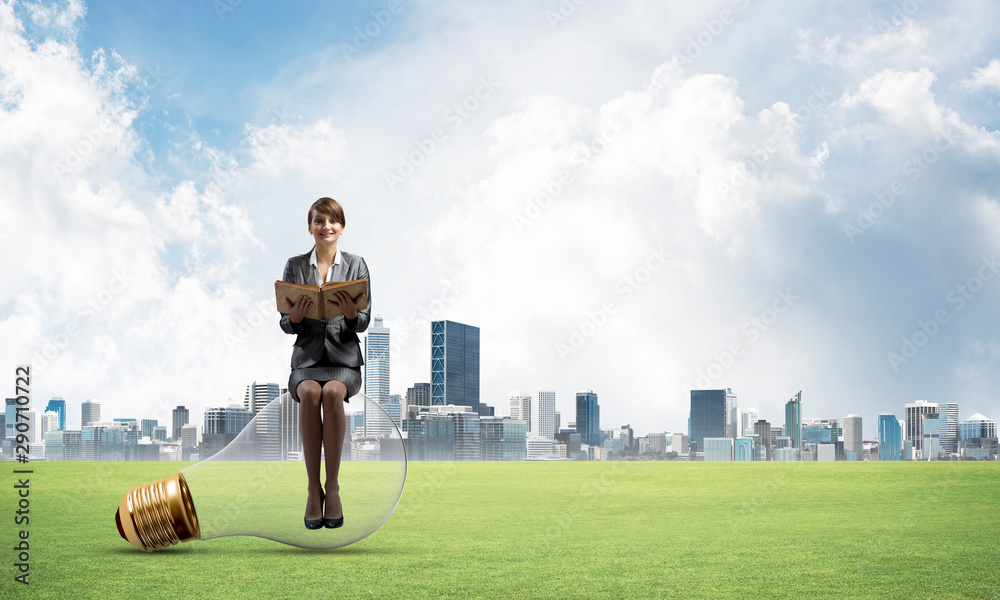 Woman with open book sitting on big light bulb