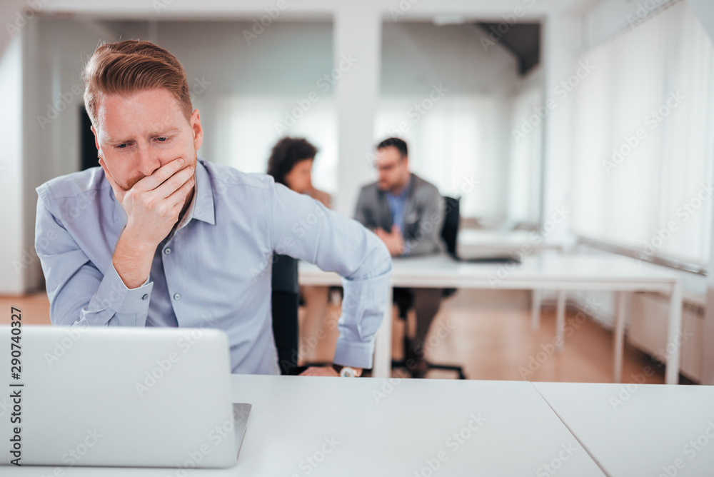 Troubled redhead businessman looking at laptop in the office, front view.