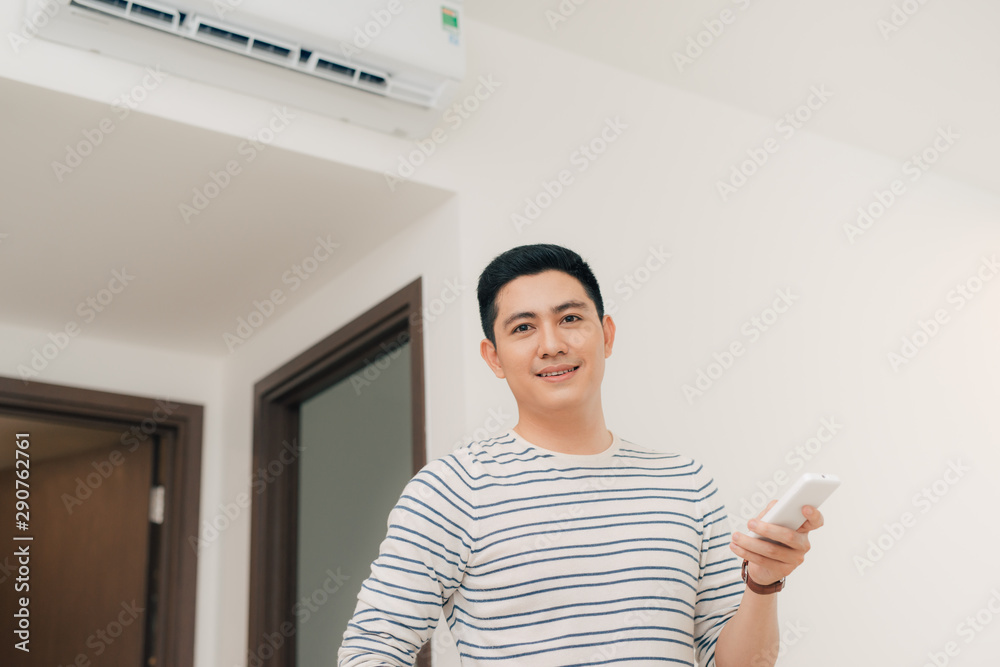 Portrait of happy man using remote control to operate air conditioner