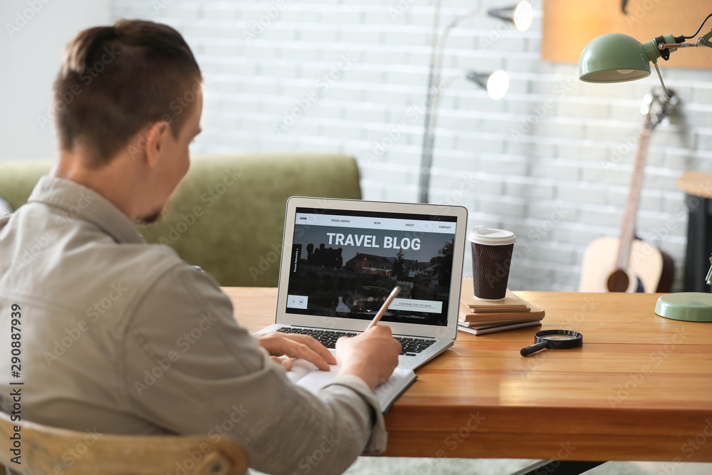 Male travel blogger with laptop at table